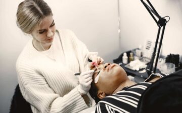 master-of-eyelash-extensions-african-girl-doing-procedure-woman-on-couch-scaled